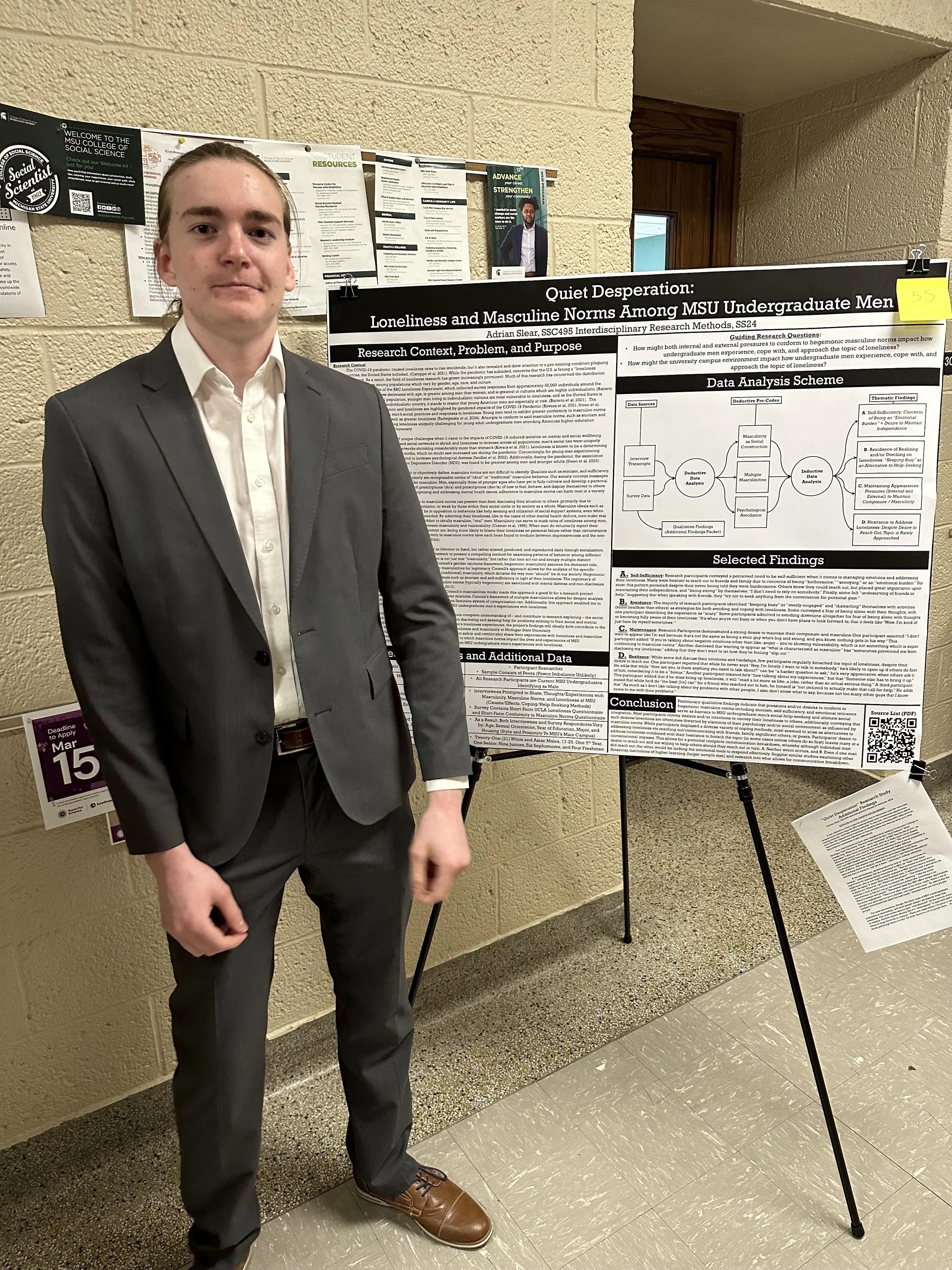 Photo of student standing in front of research poster which is one an easel. 