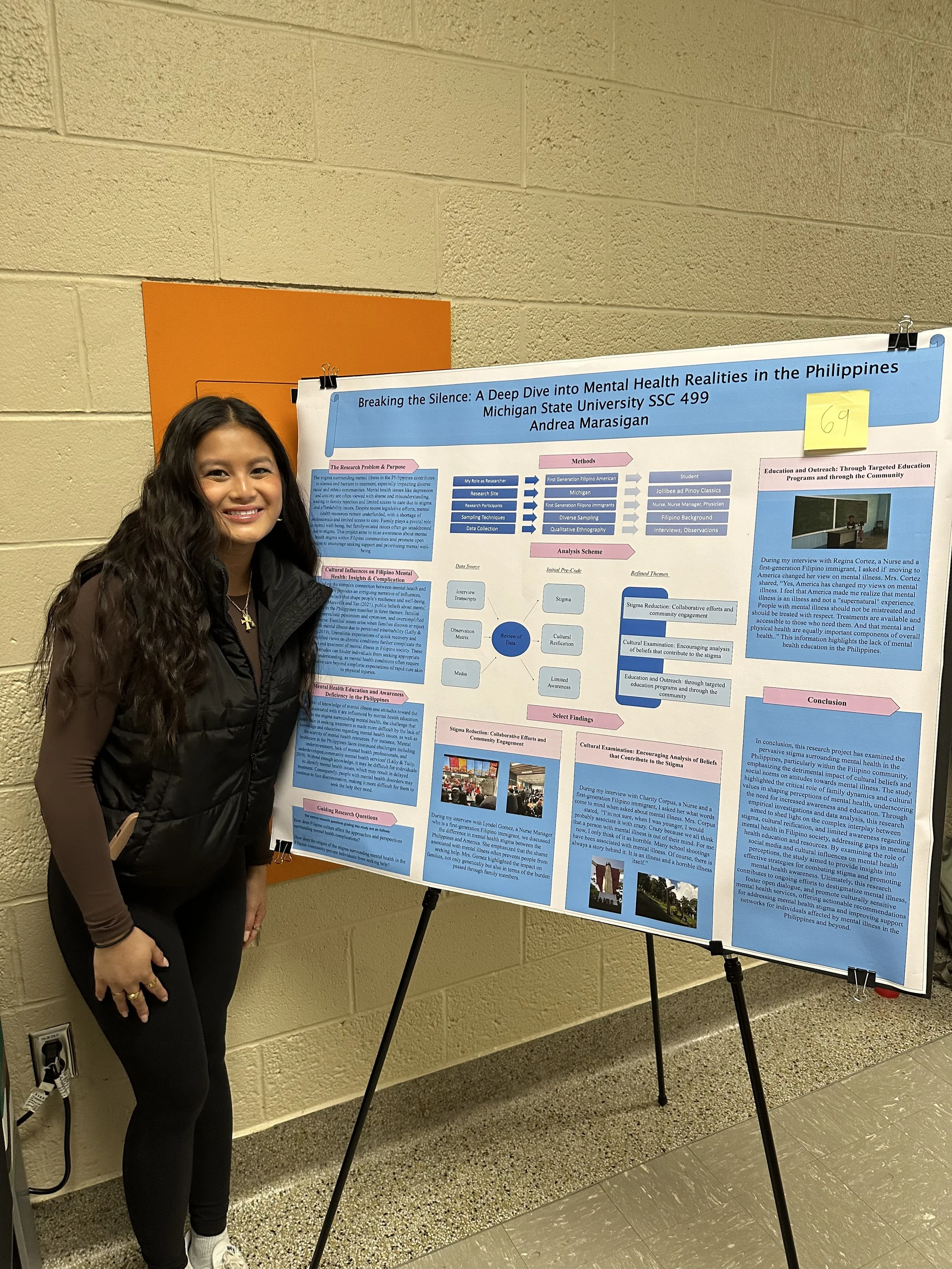 Photo of student standing in front of research poster which is one an easel. 