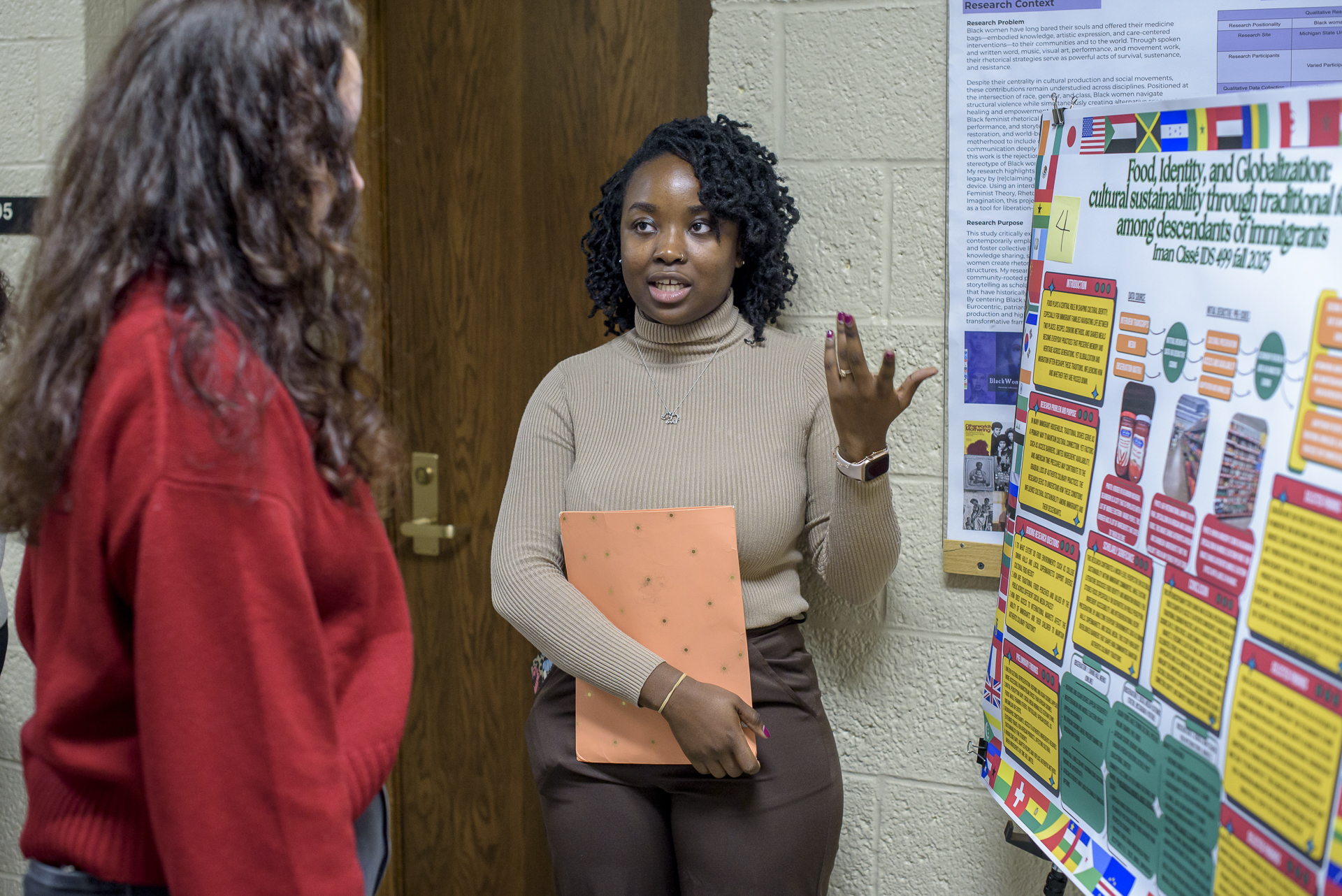 A student researcher talking to another student, with her poster next to her.