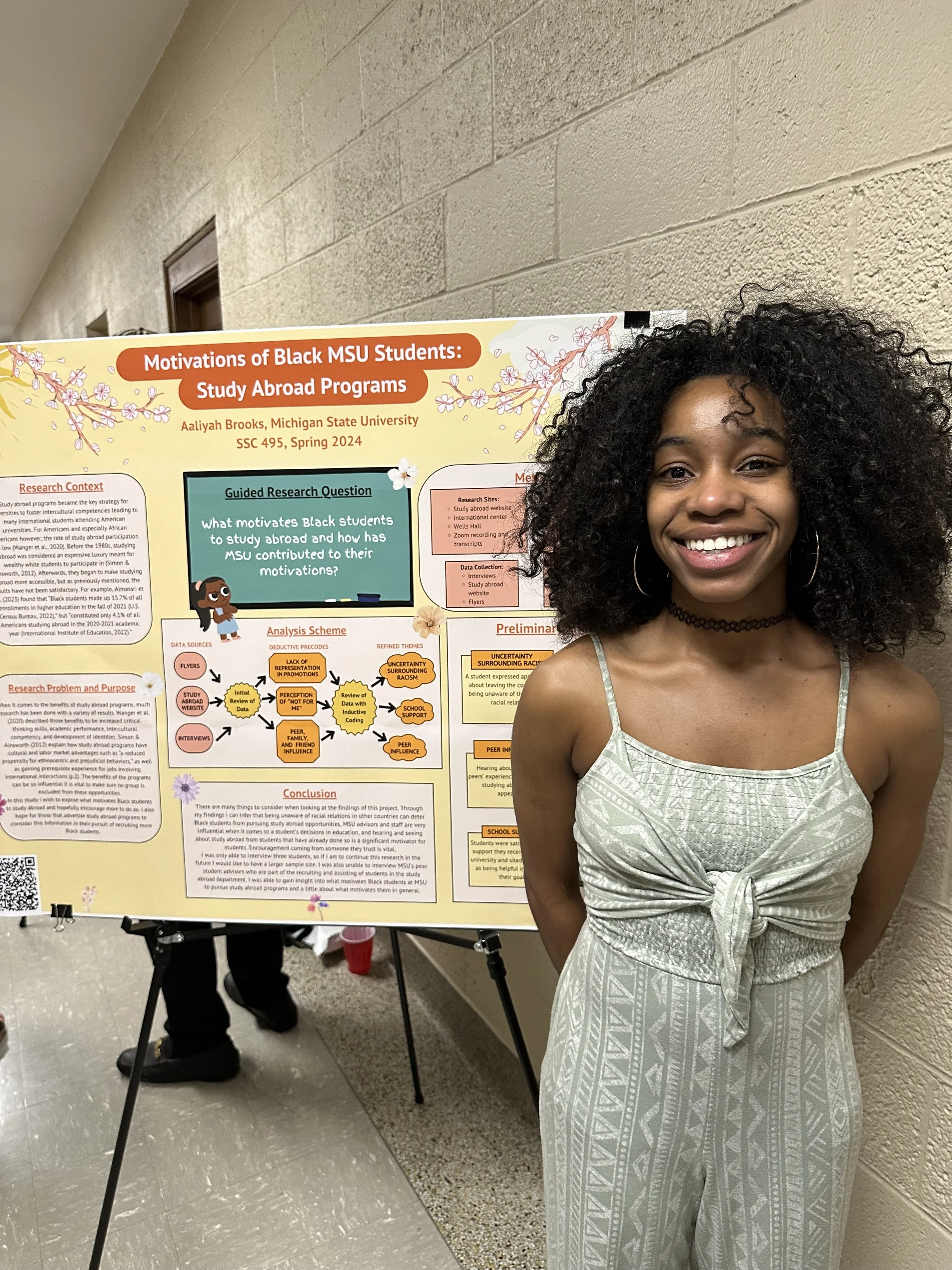 Photo of student standing in front of research poster which is one an easel. 