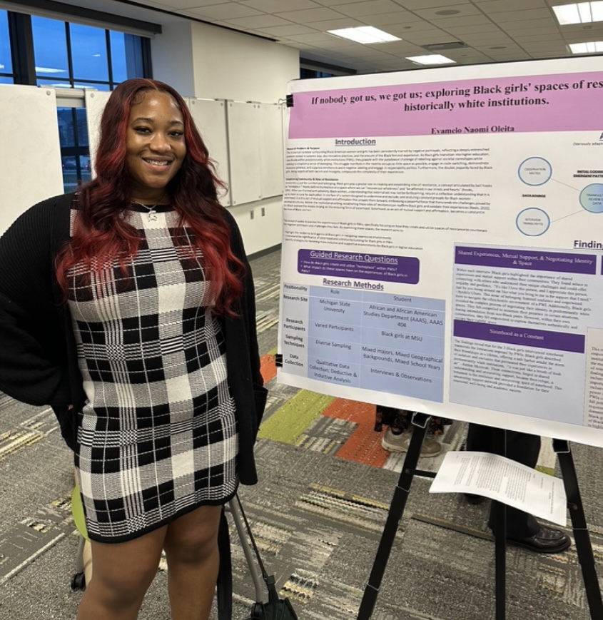 Photo of student standing in front of research poster which is one an easel. 