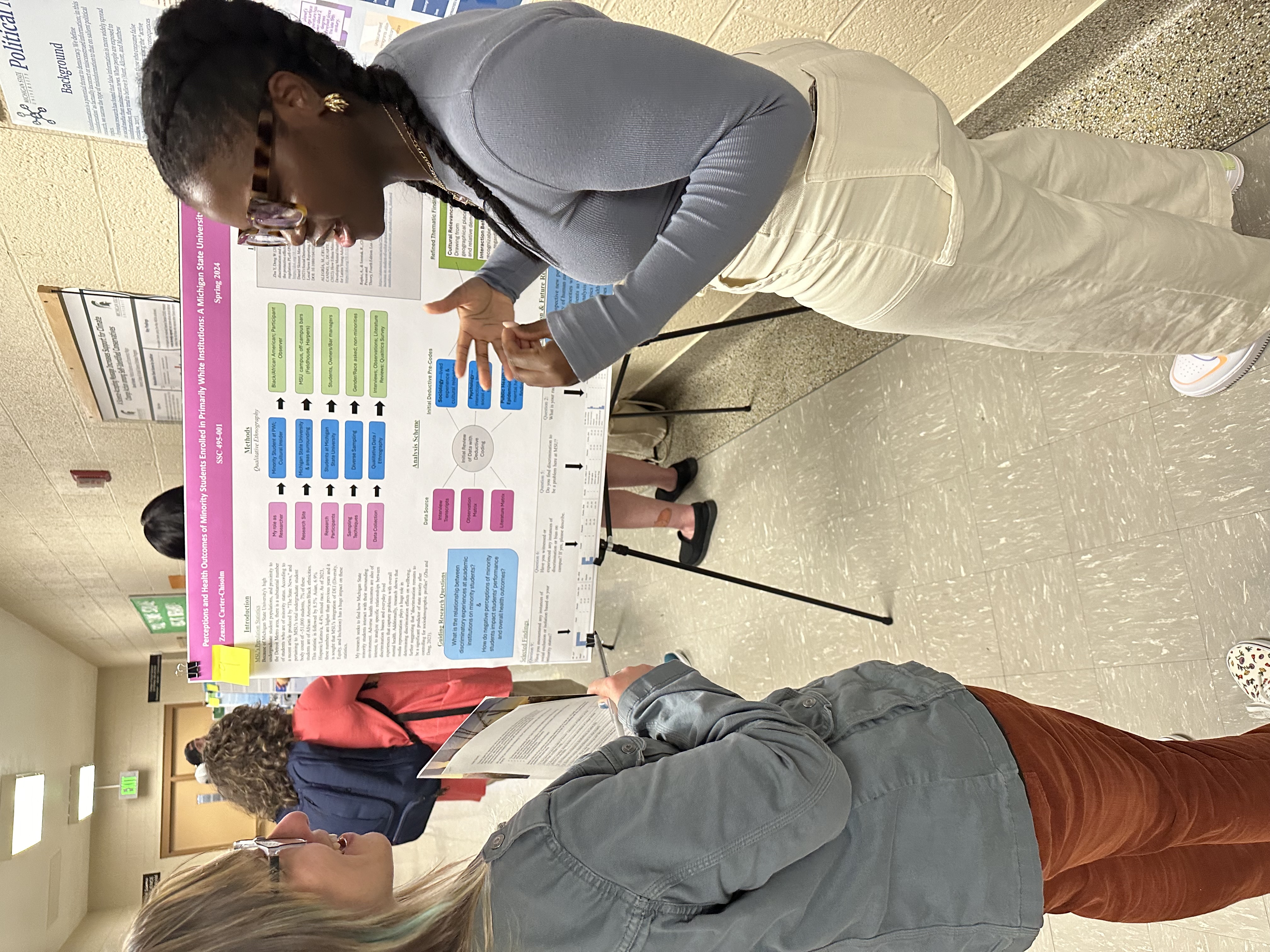 Photo of student standing in front of research poster which is one an easel. 