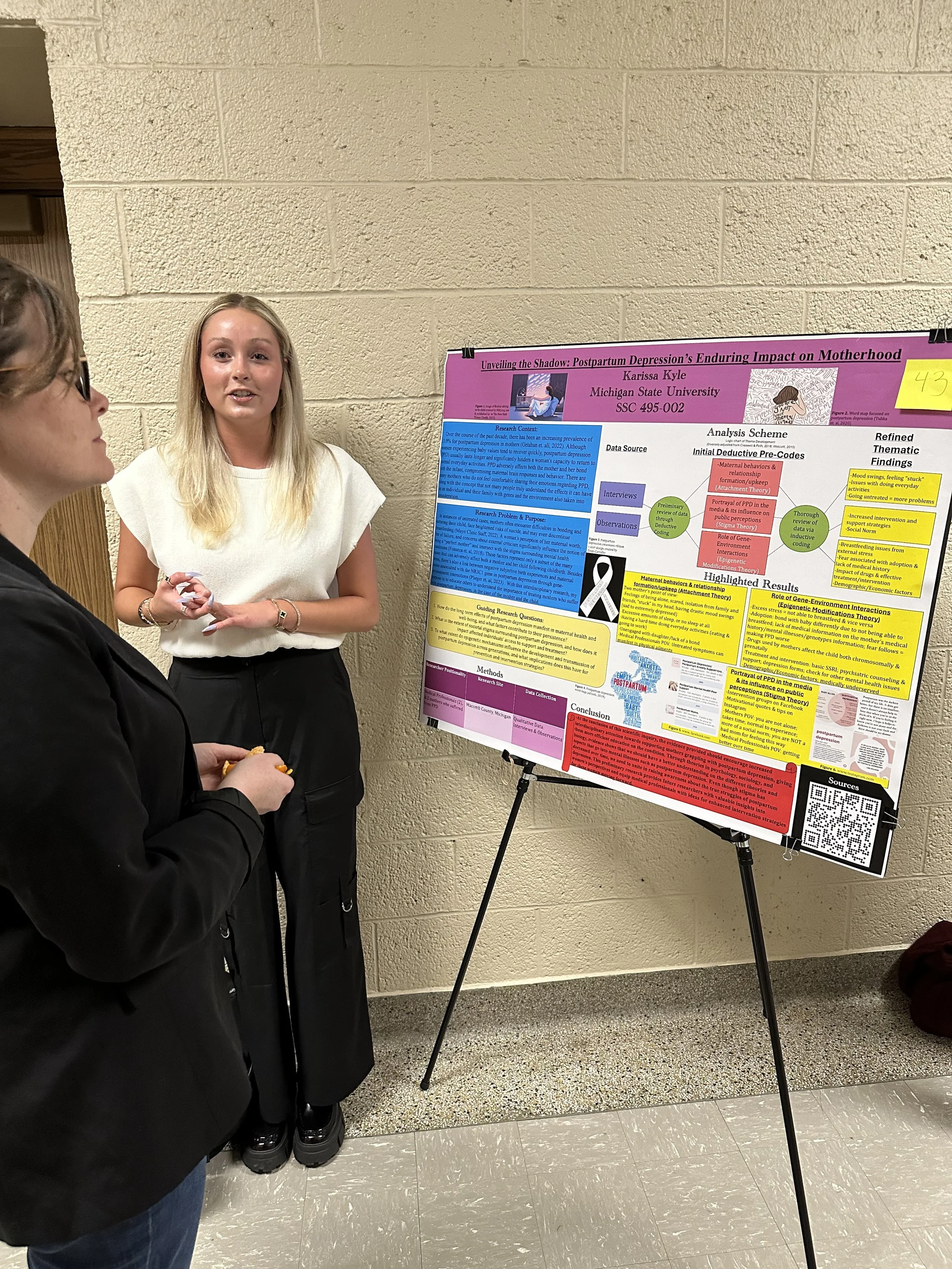 Photo of student standing in front of research poster which is one an easel. 