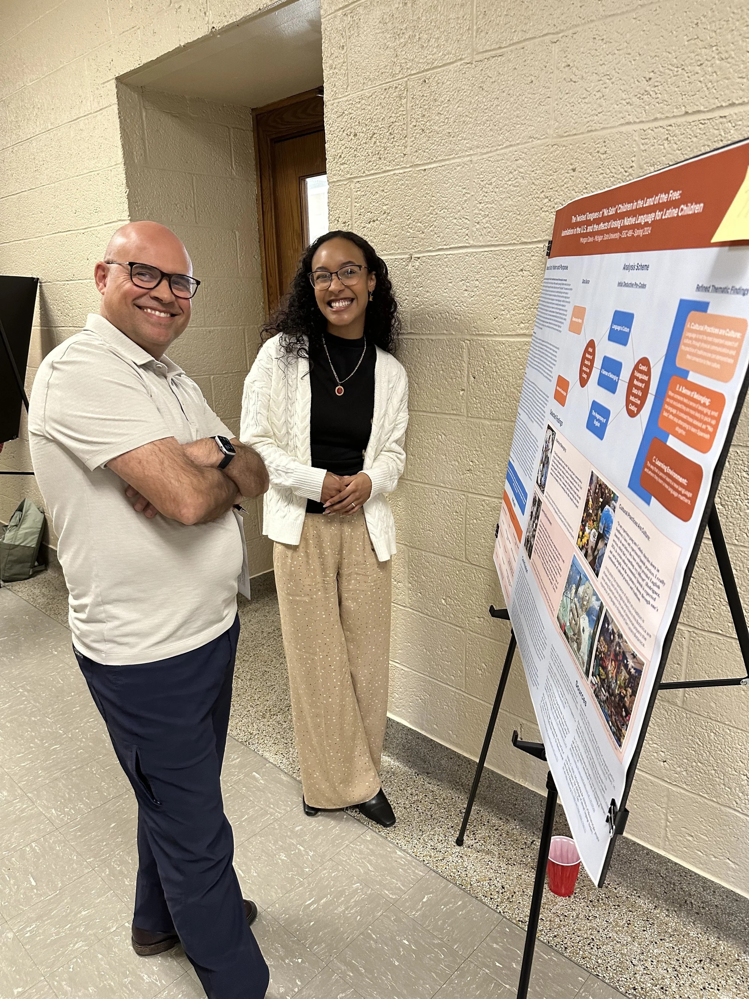 Photo of student standing in front of research poster which is one an easel. 