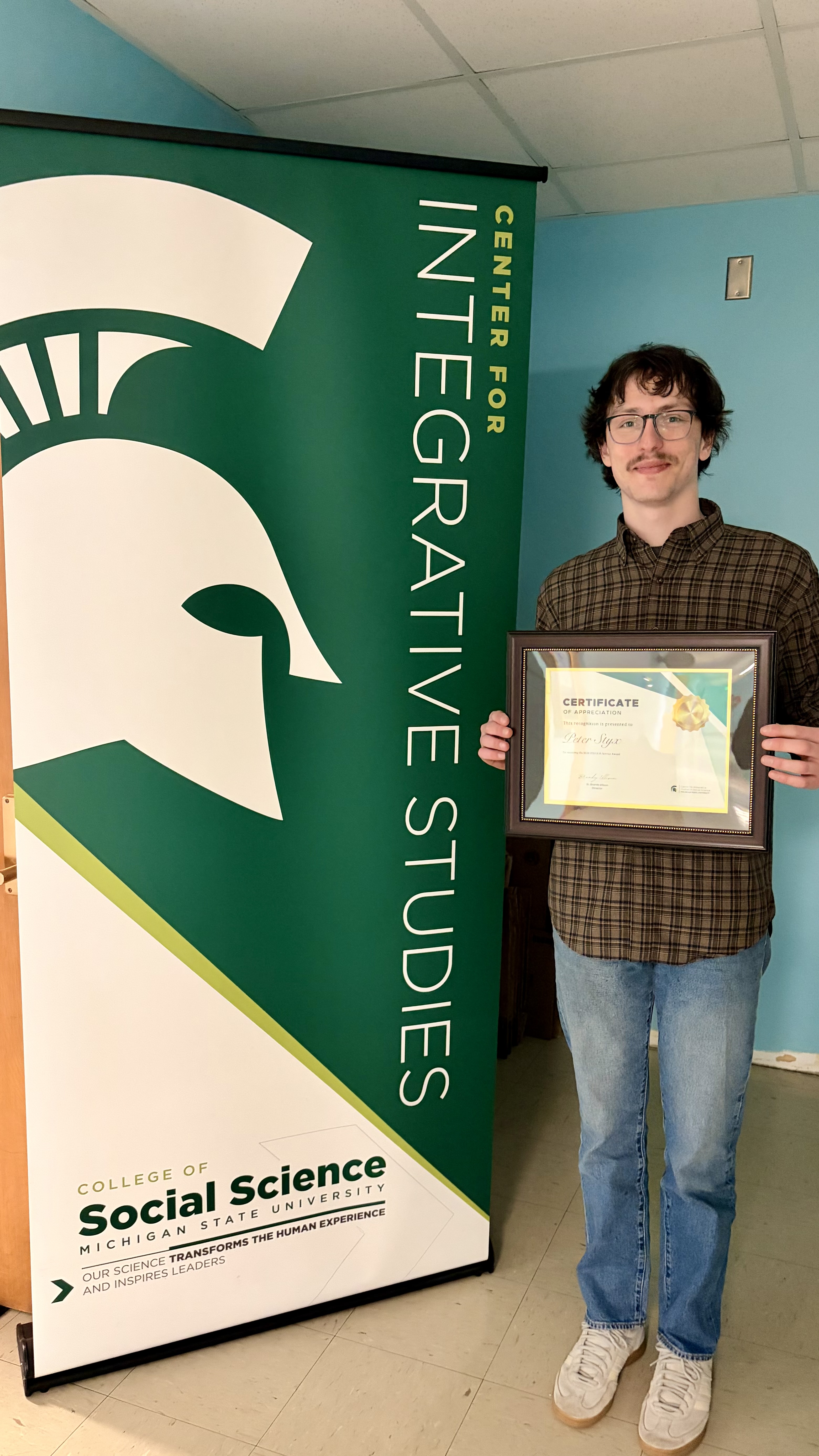 MSU student Peter Styx standing next to the Center for Integrative Studies banner.