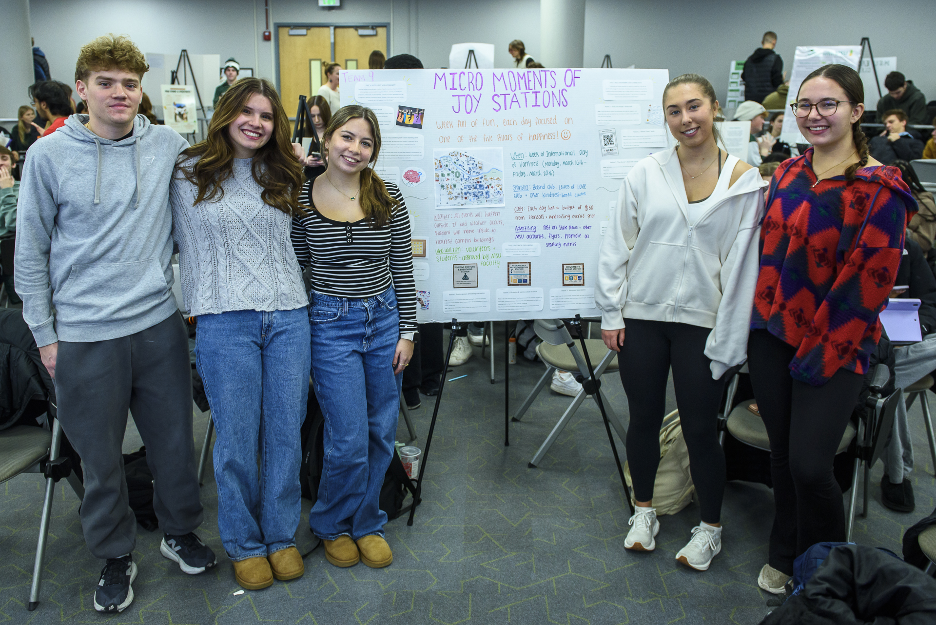 Photo of five students standing in front of their poster which is titled Mirco Moments of Joy Stations
